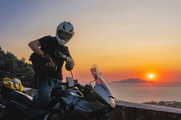 Motorcyclist man enjoy beautiful sunset, sea and mountains. Tourism and adventure. Motorcycle tour journey. copyspace for your individual text. Backpack
