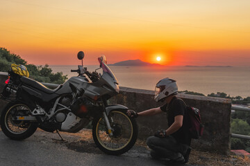 Fototapeta na wymiar Motorcyclist man loves his bike, sunset, sea and mountains. Tourism and adventure. Motorcycle tour journey. copyspace for your individual text.