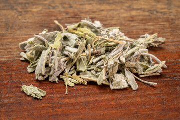 loose leaves of dry sage herb tea, a pile on a rustic weathered wood