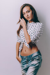 A young girl photo model in blue jeans and a white polka dot shirt poses in the studio.