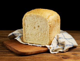 Fresh white wheat homemade bread on a wooden board on a wooden table, covered with a towel. Homemade cakes, pastries