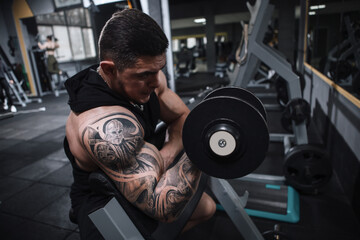 Fototapeta na wymiar Tattooed bodybuilder doing bicep curls at sports studio