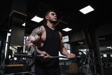 Fototapeta na wymiar Tattooed ripped weightlifter doing barbell biceps curls at gym