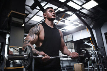 Fototapeta na wymiar Low angle shot of a tattooed bodybuilder with ripped body exercising with barbell