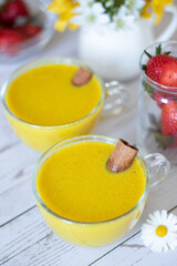 Two cups of golden latte with healing turmeric powder with curcumin ingredient. Comforting vegan dairy-free milk on a wooden table with fresh strawberries. Healthy food concept.