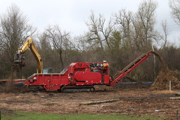 Excavator feeding tree grinding machine to turn branches, stumps and whole trees into chips on rainy spring day