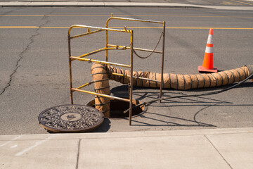 open man hole metal cover in street surrounded by safety bars and cones in middle of road with air...