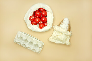 The concept of shopping without waste - bread in paper packaging and eggs in carton packages, tomatoes in a textile bag. beige background