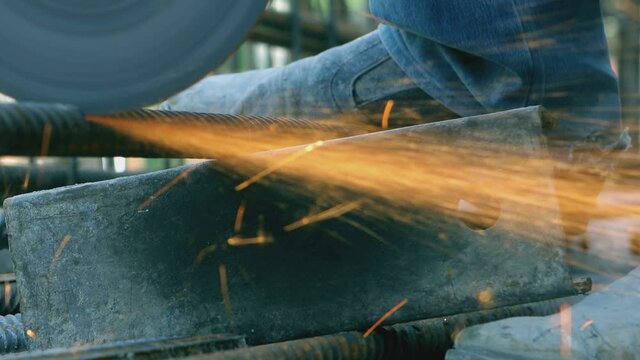 Foreman in protective gloves Using Angle Grinder and Cutting a metal pipe. Construction of building. Engineer working and grinding and sawing rebar with a grinder . Glowing bright sparks flying 
