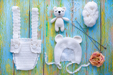 baby knitted things and toy amigurs on textured natural with multicolored light wooden background flat lay