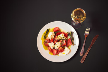 Caprese salad and glass of white wine on dark background.