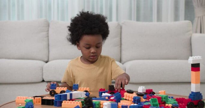 A little adorable cute African American boy making a train and the city with a colorful of bricks in living room. The boy playing a building block alone in house. Development for kids concept.