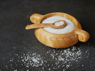 salt in a wooden cup with a spoon on the stone countertop