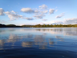 Vue sur un lac avec un effet miroir du ciel qui se reflète dans l'eau, temps légèrement nuageux, peu avant la couchée du soleil.