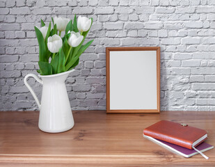 Portrait white picture frame mockup on vintage table with tulips jug vase and busines diary white brick wall background.