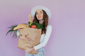 Beautiful  woman carrying a bag full of vegetables with thumbs up, isolated over pink background