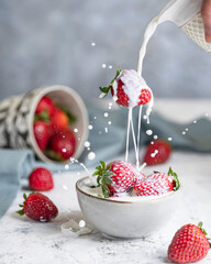 Strawberry falling into bowl with milk straw and splashing on a bowl with berries on white textured table. Levitation art studio image, motion shot. Copy space.
