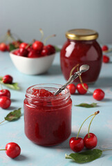 Two jars of homemade jam of sweet cherry on a light blue background. Vertical format