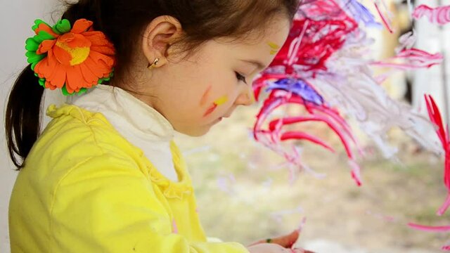 Baby face in paints close-up. Happy child draws with watercolors on the window. Children's concept. Children's emotions. Little girl with paints. Children's hand is drawn on the window pane. 