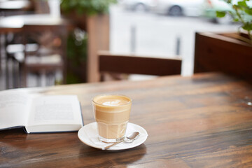 Cup of coffee and book on the table in street cafe. Cappuccino or latte in glass. Enjoying time alone