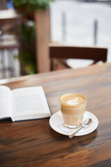 Cup of coffee and book on the table in street cafe. Cappuccino or latte in glass. Enjoying time alone