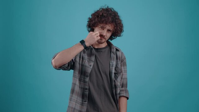 Young irritated hipster, points his finger in the face and shows the bad sign, in the studio on a turquoise background. The concept of people's lifestyle