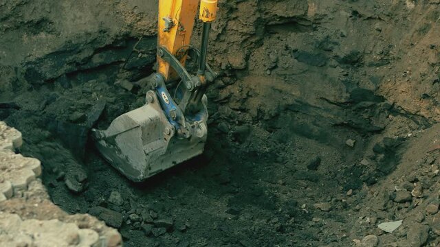 Big metallic excavator bucket scoops up ground . Ripper bucket excavating soil and rocks at a construction site . Close up bulldozer digging building foundation in slow motion. Tractor working 