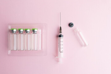Plastic syringe with injection needle, ampoules in a container, used ampoule on a pink background....