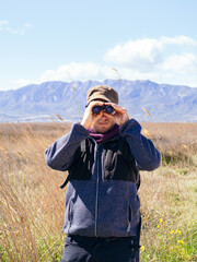 Young man hiker with a backpack looking through binoculars in the mountain