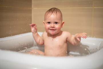 Little charming girl babe plays in the water in small inflatable baby pool located in the shower stall in bathroom, baby girl smiling and having fun