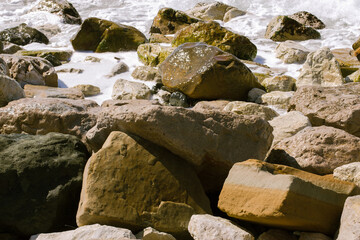 large stones of brown and gray shades on the shore are washed by the sea