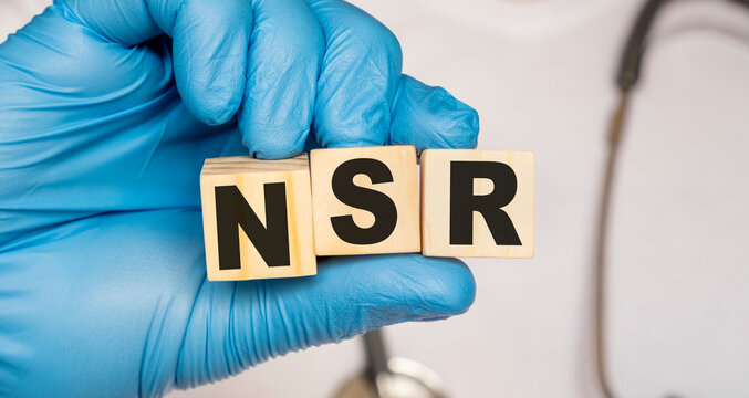 NSR Normal sinus rhythm of the heart - word from wooden blocks with letters holding by a doctor's hands in medical protective gloves. Medical concept.
