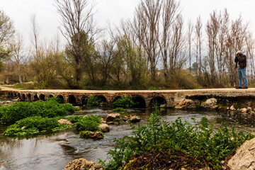 Bridge with small arches over the Serpis river next to the old train track with a photographer.
