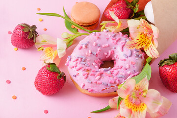 pink donat and fresh strawberries, alstroemeria flowers, beige macaroons in a paper envelope on a pink