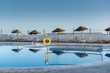 Low season, empty swimming pool with sunbeds and umbrellas reflected in the water