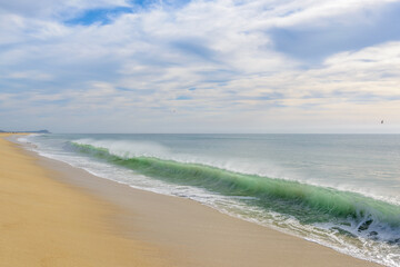 Fototapeta na wymiar green ocean water at sandy beach and clouds