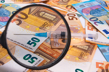 syringe close-up through a magnifying glass on the background of euro banknotes, medicine cost concept