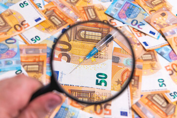 syringe close-up through a magnifying glass on the background of euro banknotes, medicine cost concept
