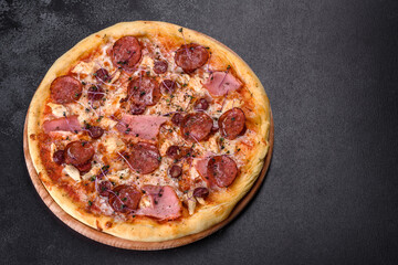 Delicious fresh oven pizza with tomatoes, salami and bacon on a dark concrete background