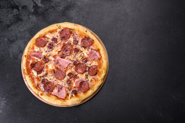 Delicious fresh oven pizza with tomatoes, salami and bacon on a dark concrete background