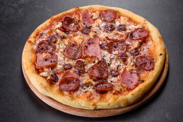 Delicious fresh oven pizza with tomatoes, salami and bacon on a dark concrete background