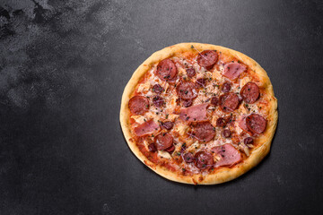 Delicious fresh oven pizza with tomatoes, salami and bacon on a dark concrete background