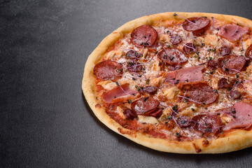 Delicious fresh oven pizza with tomatoes, salami and bacon on a dark concrete background
