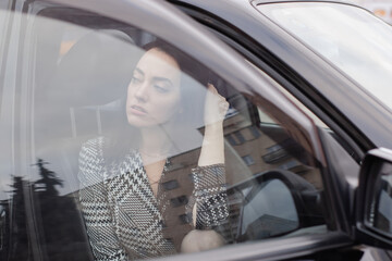 portrait of attractive brunette in grey checkered dress in a black car. girl in automobile....