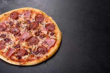Delicious fresh oven pizza with tomatoes, salami and bacon on a dark concrete background