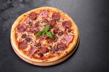 Delicious fresh oven pizza with tomatoes, salami and bacon on a dark concrete background