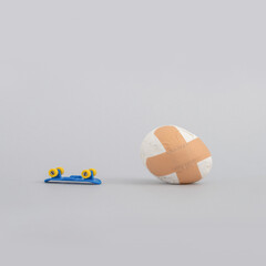 Creative food concept with broken egg with adhesive bandage and skateboard on grey background