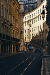 Fototapeta premium A street in Lisbon, Portugal. Cars and lines for the trolleybus. Curved buildings and sunset light.