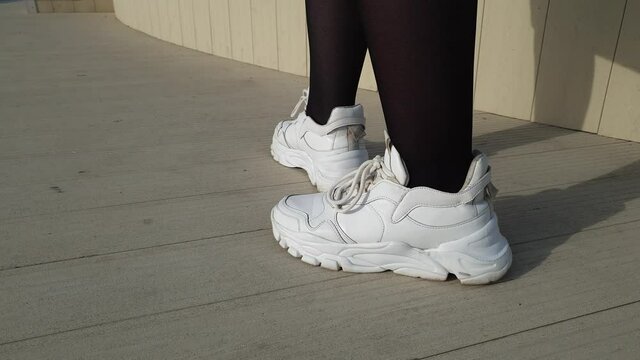 women's legs in nylon black pantyhose close up, woman in black stockings , white sneakers and gray skirt walking in the park on a sunny day, foot fetish