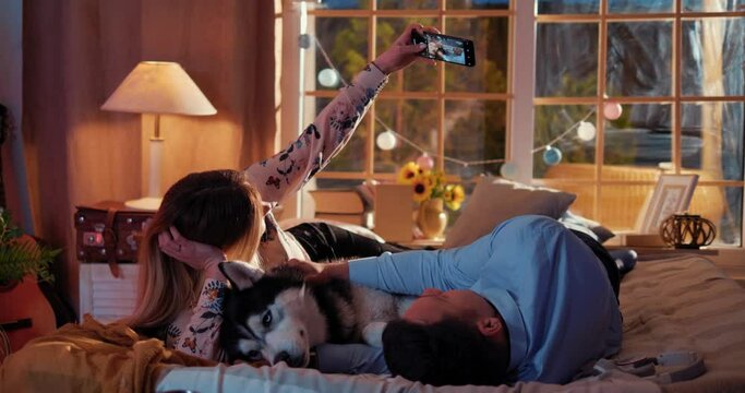 Couple take a selfie with dog on smartphone while lying on the bed in the bedroom